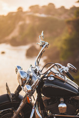 Fototapeta premium Old vintage motorcycle standing on the edge of cliff in warm sunlight at sunrise, shiny details of bike close-up