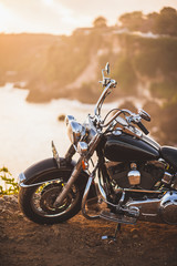 Altes Oldtimer-Motorrad, das bei Sonnenaufgang in warmem Sonnenlicht am Rand einer Klippe steht, glänzende Details der Fahrradnahaufnahme