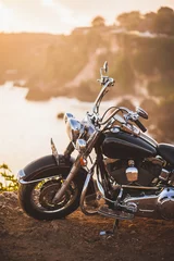 Fototapete Dunkelbraun Altes Oldtimer-Motorrad, das bei Sonnenaufgang in warmem Sonnenlicht am Rand einer Klippe steht, glänzende Details der Fahrradnahaufnahme