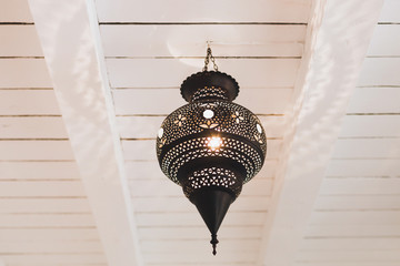 Old vintage lamp in moroccan style hanging on white wooden roof