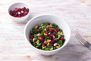 Warm kale salad with brown rice, dried cranberries and nuts on a light background. Delicious healthy diet food