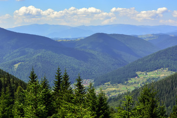 landscapes of mountains covered with dense coniferous forest, against a blue sky with clouds