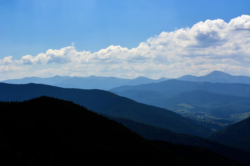 Obraz premium landscapes of mountains covered with dense coniferous forest, against a blue sky with clouds