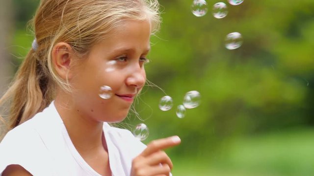 Nine-year-old girl playing with soap bubbles outdoor. Slow motion. 