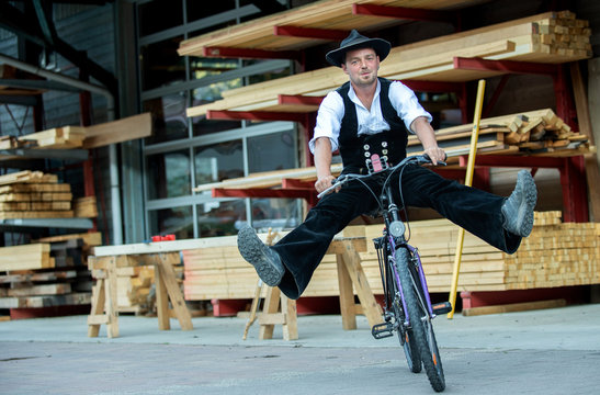 Zimmermann  in Arbeitskluft,  vor Holzlager, hat Spa&szlig; auf dem Fahrrad
