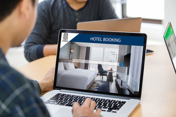 Man working on laptop, searching for lodging using on-line web service, booking a hotel on website...