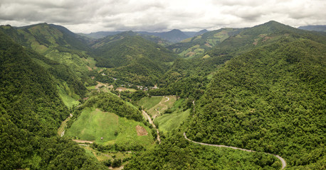 Aerial view of countryside road passing through the lush greenery and foliage tropical rain forest mountain landscape in the Northern Thailand