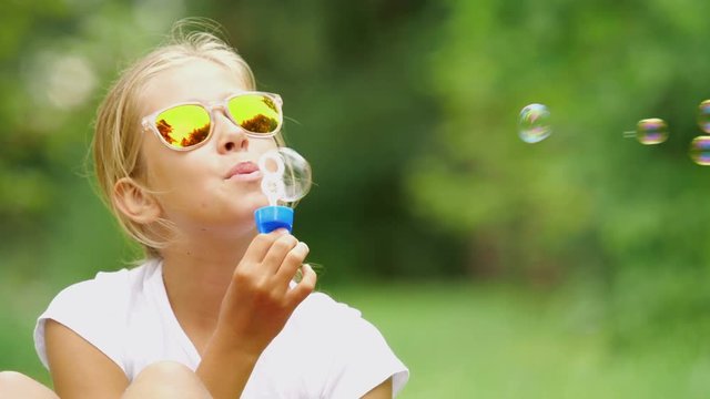 Nine-year-old girl plays with soap bubbles in the summer garden.