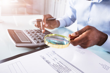 Businessman Holding Magnifying Glass Over Invoice