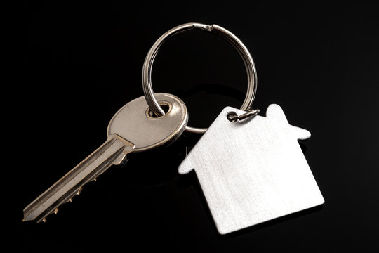 Real estate investment and buying new apartment concept with close up on house key with home shaped keychain on black background