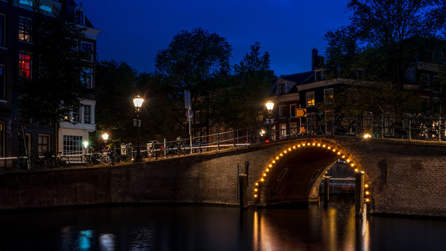 Dutch landmarks and travel destinations in the Nederlands concept with a bridge over a canal in Amsterdam illuminated by light bulbs at night