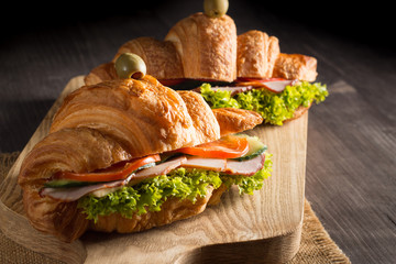 Photo of tasty and fresh croissant sandwich with salad, ham, cheese, tomatoes on wooden background. Morning breakfast concept. Healthy and fast food.
