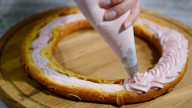 Half of a Paris Brest cake. Background: a pastry bag filling with whipped cream.