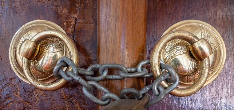 Closeup of two antique copper ornate door knockers over an aged wooden ornate door closed with rusted chain, Eyup Sultan Mosque, Istanbul, Turkey