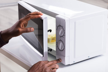 Man's Hand Heating Food In Microwave Oven