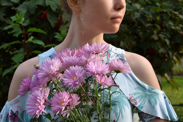 Young woman is holding pink chrysanthemum flowers on a sunny day in the park