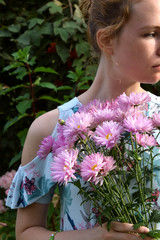 Young woman is holding pink chrysanthemum flowers on a sunny day in the park