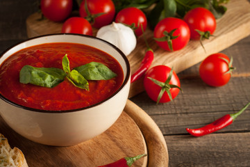 Fresh, healthy tomato soup with basil, pepper, garlic, tomatoes and bread on wooden background. Spanish gazpacho soup.