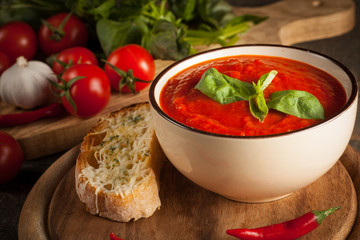 Fresh, healthy tomato soup with basil, pepper, garlic, tomatoes and bread on wooden background. Spanish gazpacho soup.