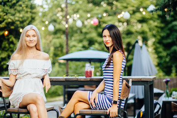 Сlose up pictures of two woman’s relaxing on party drinking summer cold tasty cocktails in outdoor cafe in park, vacation fun mood. Summer holidays, people, friendship and vacation concept.