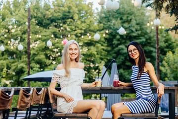 Two women relaxing on party, laughing, drinking summer cold tasty cocktails in outdoor cafe in park, vacation fun mood. Summer holidays, people, friendship and vacation concept.