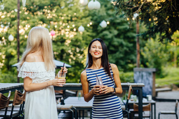 Two women relaxing on party, go clubbing. laughing, drinking summer cold tasty cocktails in outdoor...