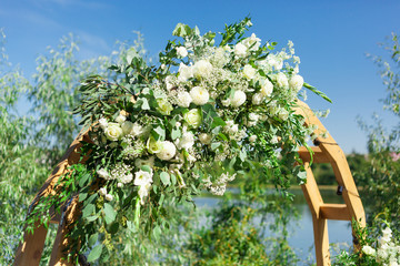 Part of beautiful round wedding arch decorated with flowers and greenery near lake or river outdoors, element. Decorations for wedding ceremony in open air