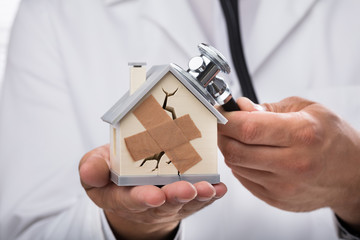 Doctor examining broken house with stethoscope