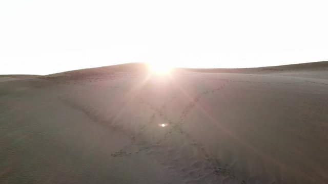 Aerial: sunset in a desert. Camera flies to the setting sun in a desert with beautiful sunlight and orange sky. Texture of sand dunes. Gran Canaria