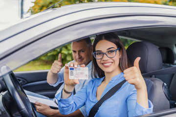 Driving school. Beautiful young woman successfully passed driving school test. She looking sitting in car, looking at camera and holding driving license in hand.