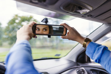 Adjusting the rear view mirror. Woman adjusts the rear view mirror with her hand. Happy young woman driver looking adjusting rear view car mirror, making sure line is free visibility is good