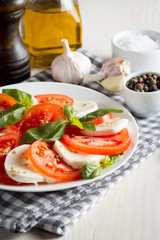 Photo of Caprese Salad with tomatoes, basil, mozzarella, olives and olive oil on wooden background. Italian traditional caprese salad ingredients. Mediterranean, organic and natural food concept.