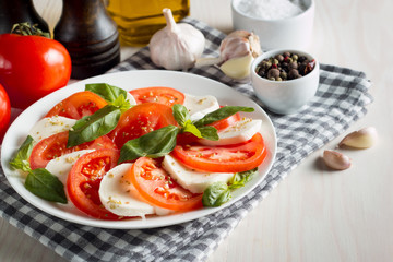 Photo of Caprese Salad with tomatoes, basil, mozzarella, olives and olive oil on wooden background. Italian traditional caprese salad ingredients. Mediterranean, organic and natural food concept.