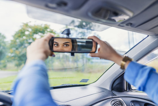 Adjusting the rear view mirror. Woman adjusts the rear view mirror with her hand. Happy young woman driver looking adjusting rear view car mirror, making sure line is free visibility is good