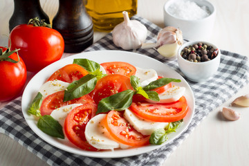 Photo of Caprese Salad with tomatoes, basil, mozzarella, olives and olive oil on wooden background. Italian traditional caprese salad ingredients. Mediterranean, organic and natural food concept.