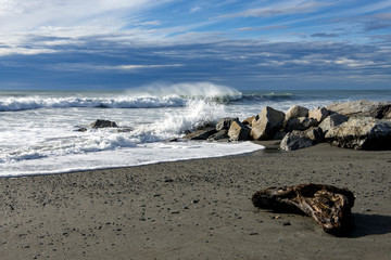 Fototapeta na wymiar Driftwood by rocks on Hokitika beach