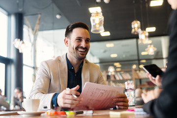 Portrait of a young successful businessman in a coffee shop analyzing paper work with his colleagues.