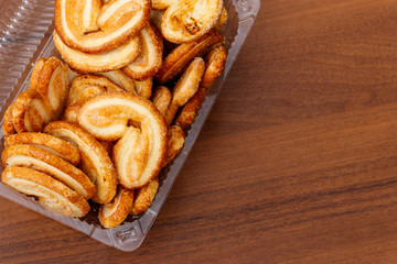 Palmier biscuits - french cookies made of puff pastry (also called palm leaves, elephant ears or french hearts) packed in plastic box on wooden table