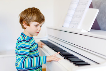 Cute healthy little kid boy playing piano in living room or music school. Preschool child having fun with learning to play music instrument. Education, skills concept