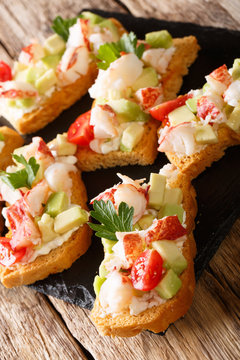Tasty toasts with lobster, avocado, tomato and cream cheese close-up on the table. vertical