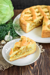 Homemade pie with cabbage, carrot, onion and meat on wooden background.