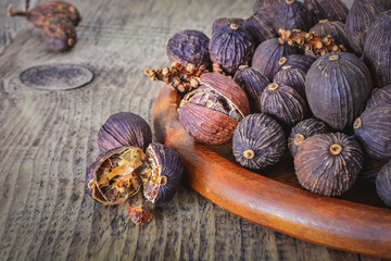 Black cardamom pods with open shell on wooden plate and Indian spice on background.