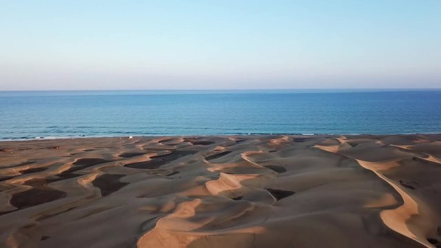 Horizon landscape of beautiful desert with sand dunes, the ocean on the background and blue sky in sunset light. Wonderful peaceful nature landscape, aerial. Gran Canaria