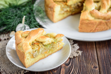 Homemade pie with cabbage, carrot, onion and meat on wooden background.