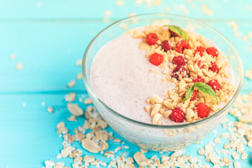 Smoothie bowl with oats, raspberry and peanut butter on blue wooden background. Healthy summer breakfast.