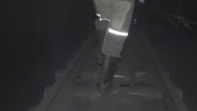 Legs of a miner walking along a tunnel in a coal mine. View from the back