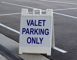 A white and blue valet parking sign in the parking lot.