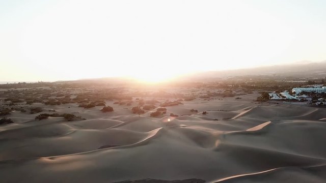 Aerial: beautiful landscape of a desert with sand dunes in sunset light. The sun is setting in a desert, camera flies down. Gran Canaria