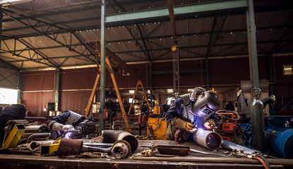 Front view of a industry work space with people in protective uniform cutting metal pipes.
