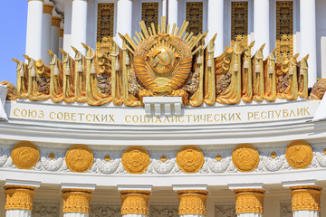 Gilded coat of arms of Soviet Union over colonnade of pavilion Central on Exhibition of...